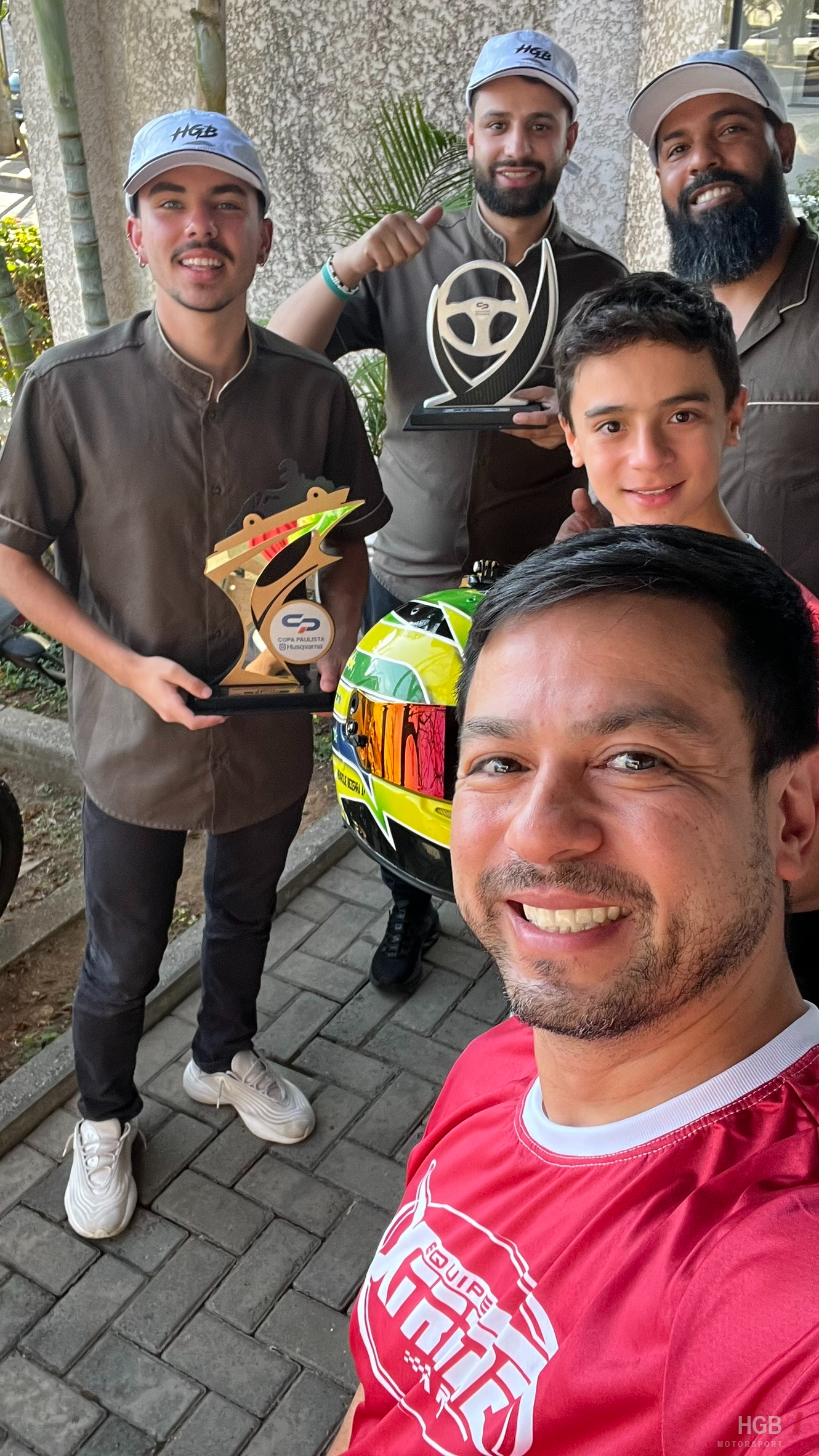 Equipe da barbearia usando os bonés da marca HGB ao lado de Henrique e dos troféus